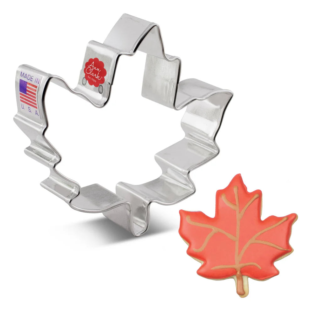 Silver maple leaf cookie cutter with a red maple leaf-shaped cookie on a white background