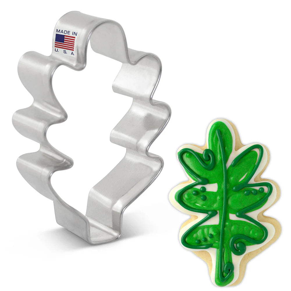 Metal leaf-shaped cookie cutter with a cookie shaped like a green leaf on a white background