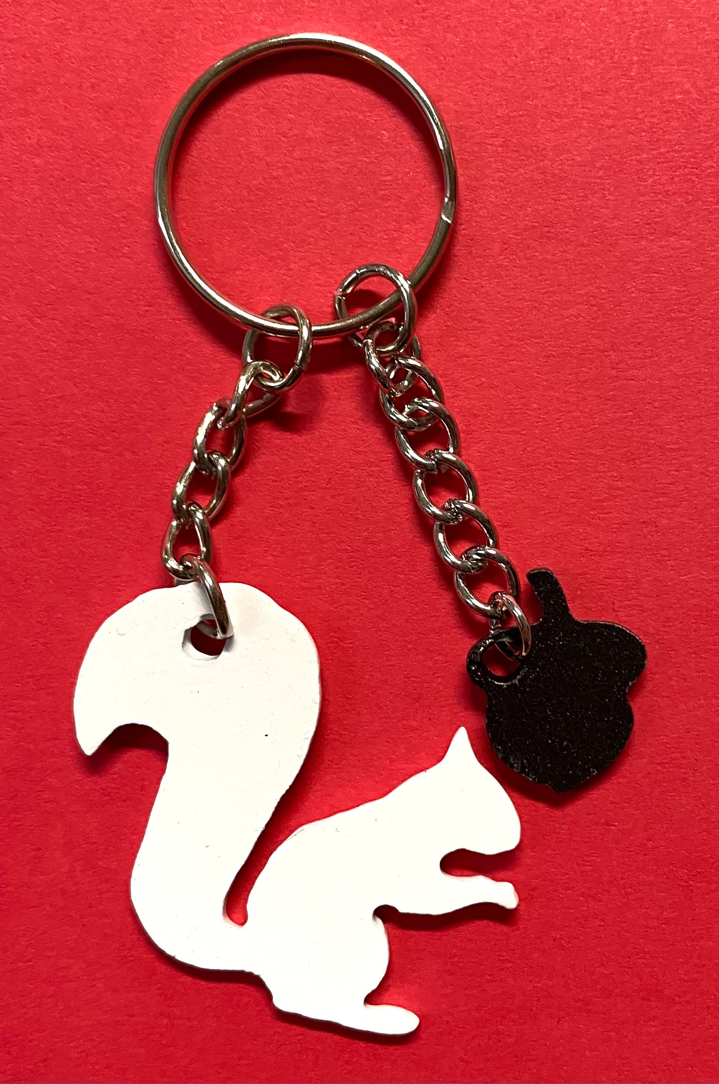 A metal die-cut key chain in the shape of a white squirrel with an acorn embellishment on a red background.