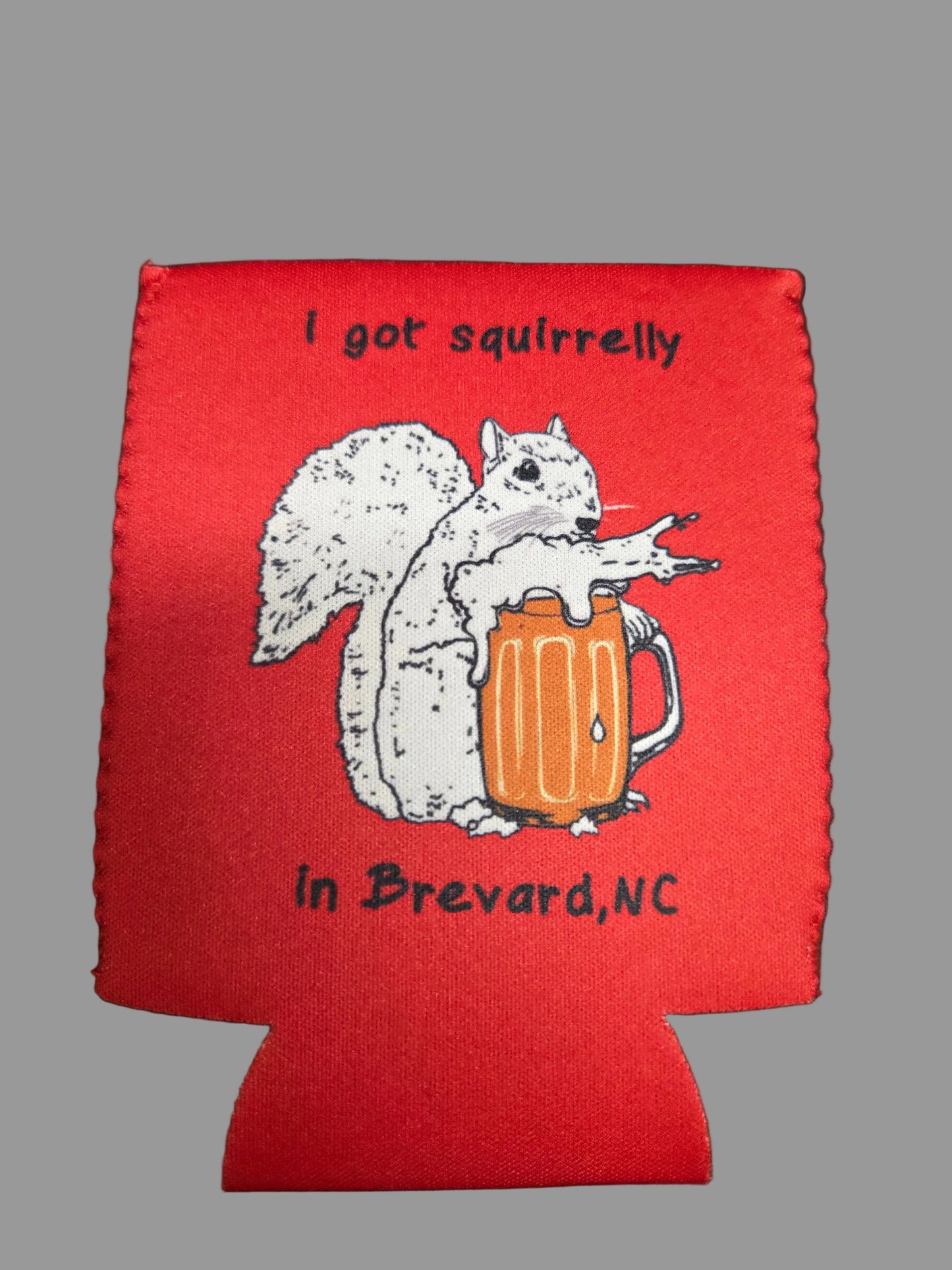 Red can cooler with a graphic of a squirrel holding a pint with the text 'I got squirrelly in Brevard, NC.
