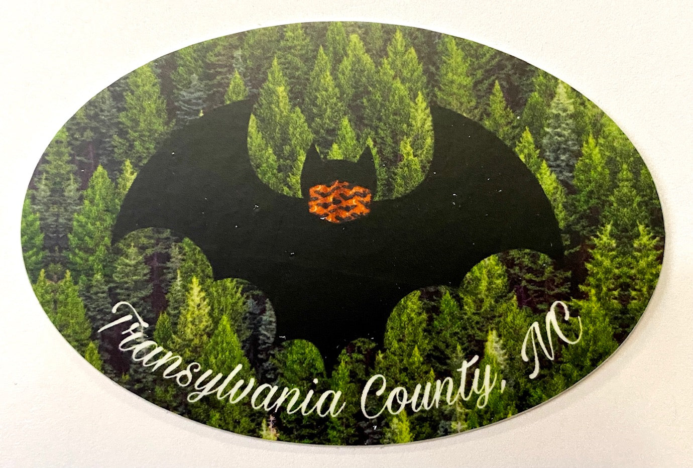 A vinyl decal with a black bat design wearing a face mask over a green forest background, with text 'Transylvania County, NC'.