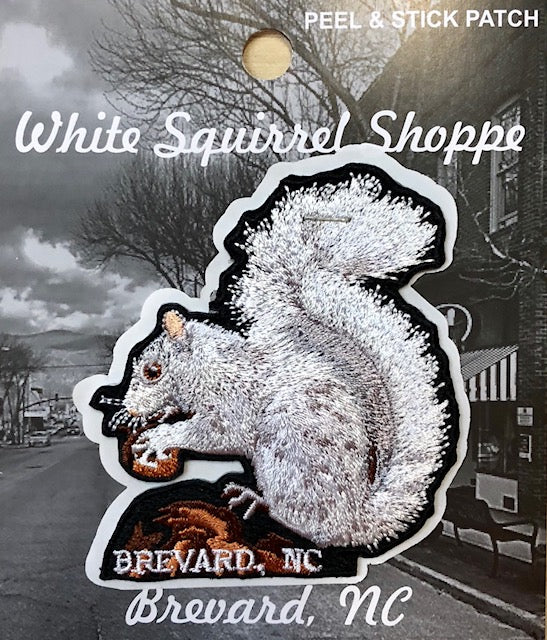 Embroidered patch depicting a white squirrel with an acorn sitting on a rock, a Peel & Stick Patch. Includes 'Brevard, NC' text below.