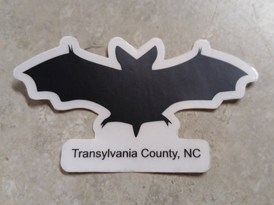 A black and white sticker in the shape of a bat with the text 'Transylvania County, NC' on the bottom.