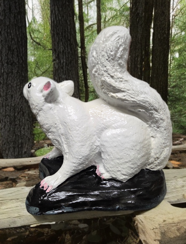 White squirrel statue on a black base in a forest setting