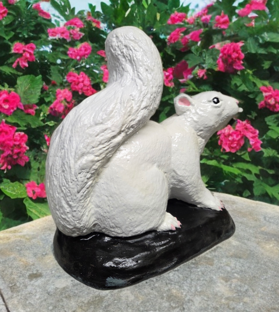White ceramic squirrel figurine on a black base with pink flowers in the background