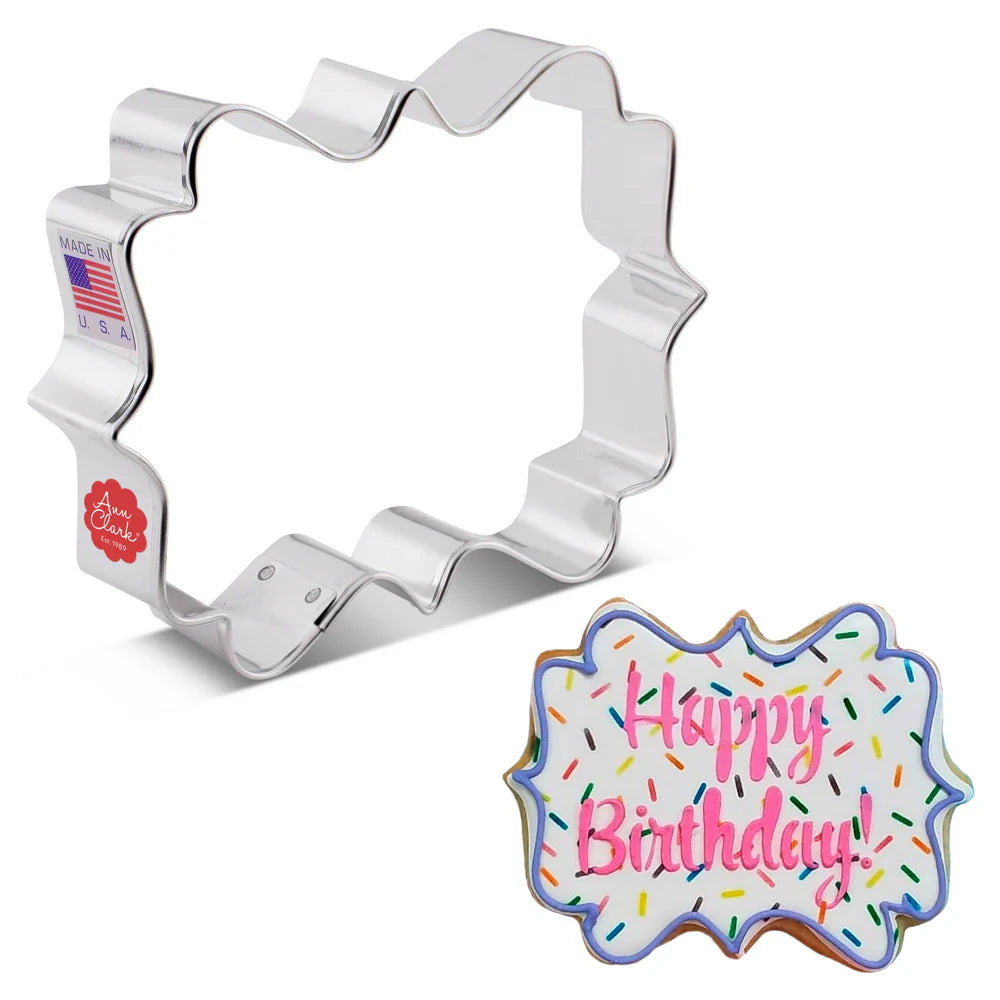Metallic cookie cutter shaped like a birthday cake with 'Happy Birthday!' text on a white background