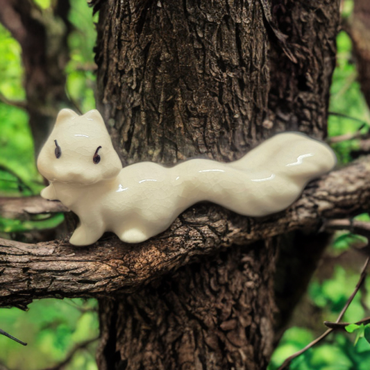 White ceramic squirrel figurine displayed on a tree branch with a natural background.