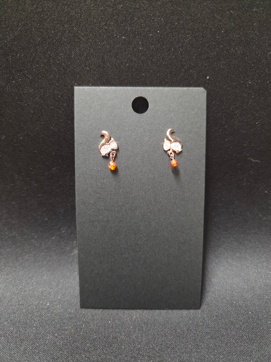 Pair of small stud earrings with a white squirrel and a gem for the nut he's carrying.on a black card against a dark background