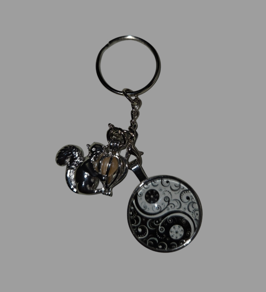 Keychain with yin yang design and small figures on a gray background