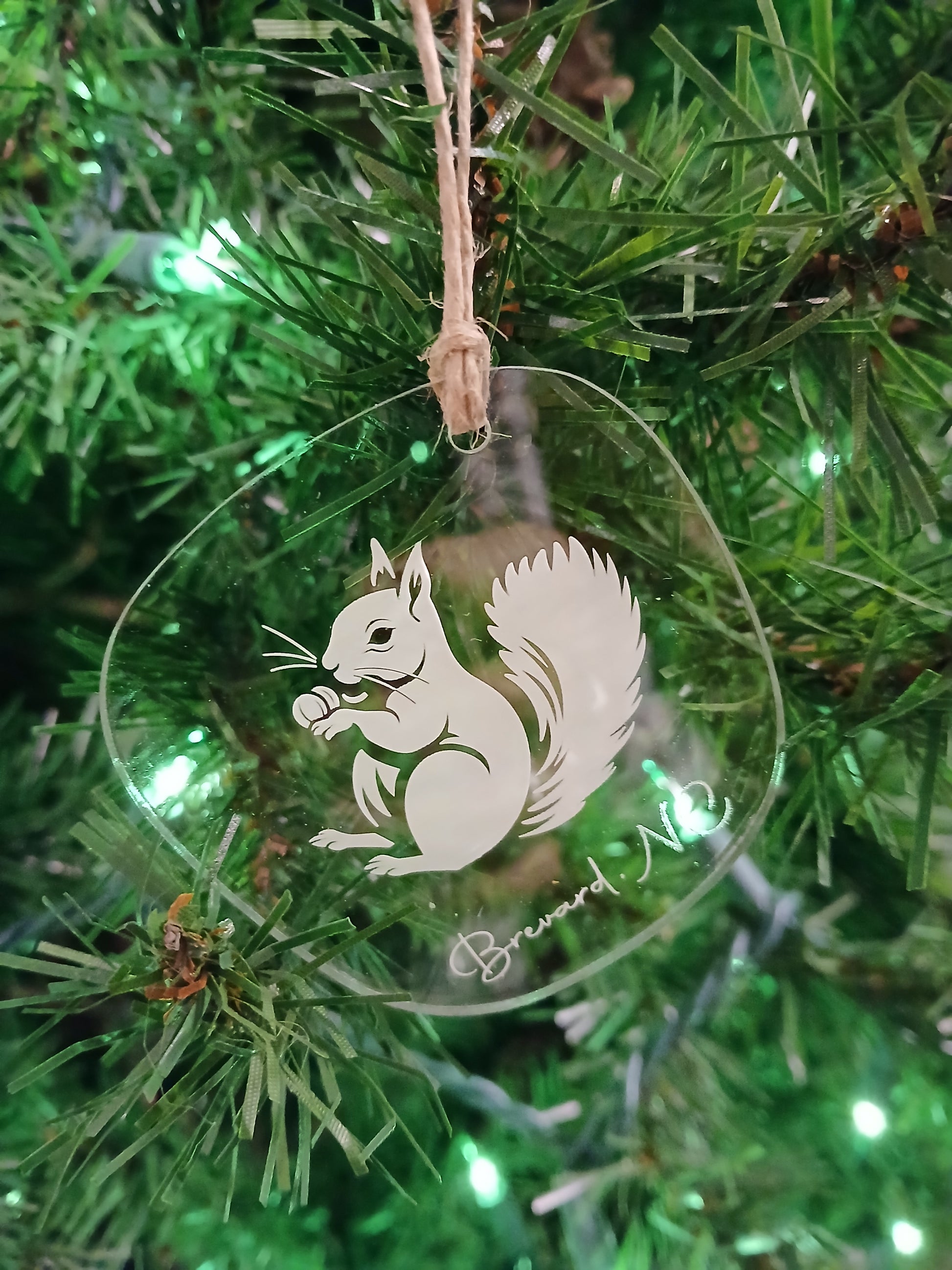A white squirrel acrylic ornament with the text 'Brevard, NC' hanging on a Christmas tree.