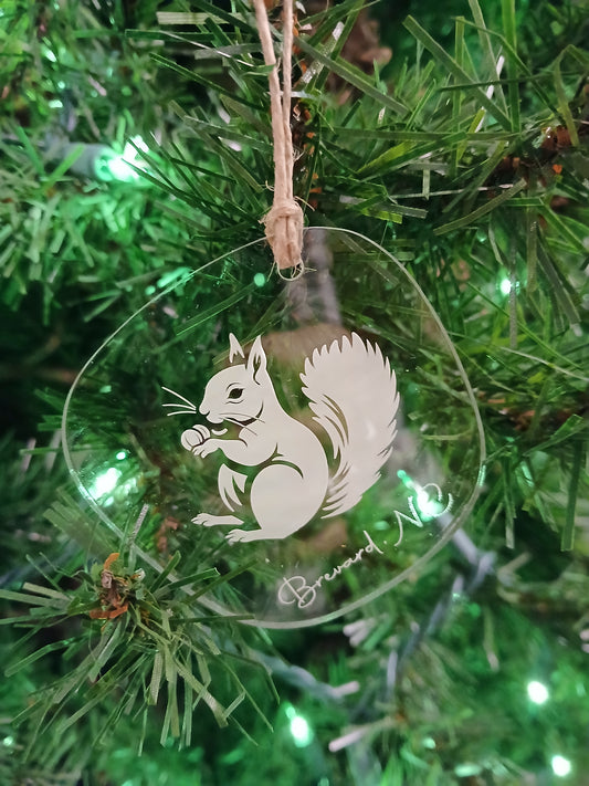 A white squirrel acrylic ornament with the text 'Brevard, NC' hanging on a Christmas tree.