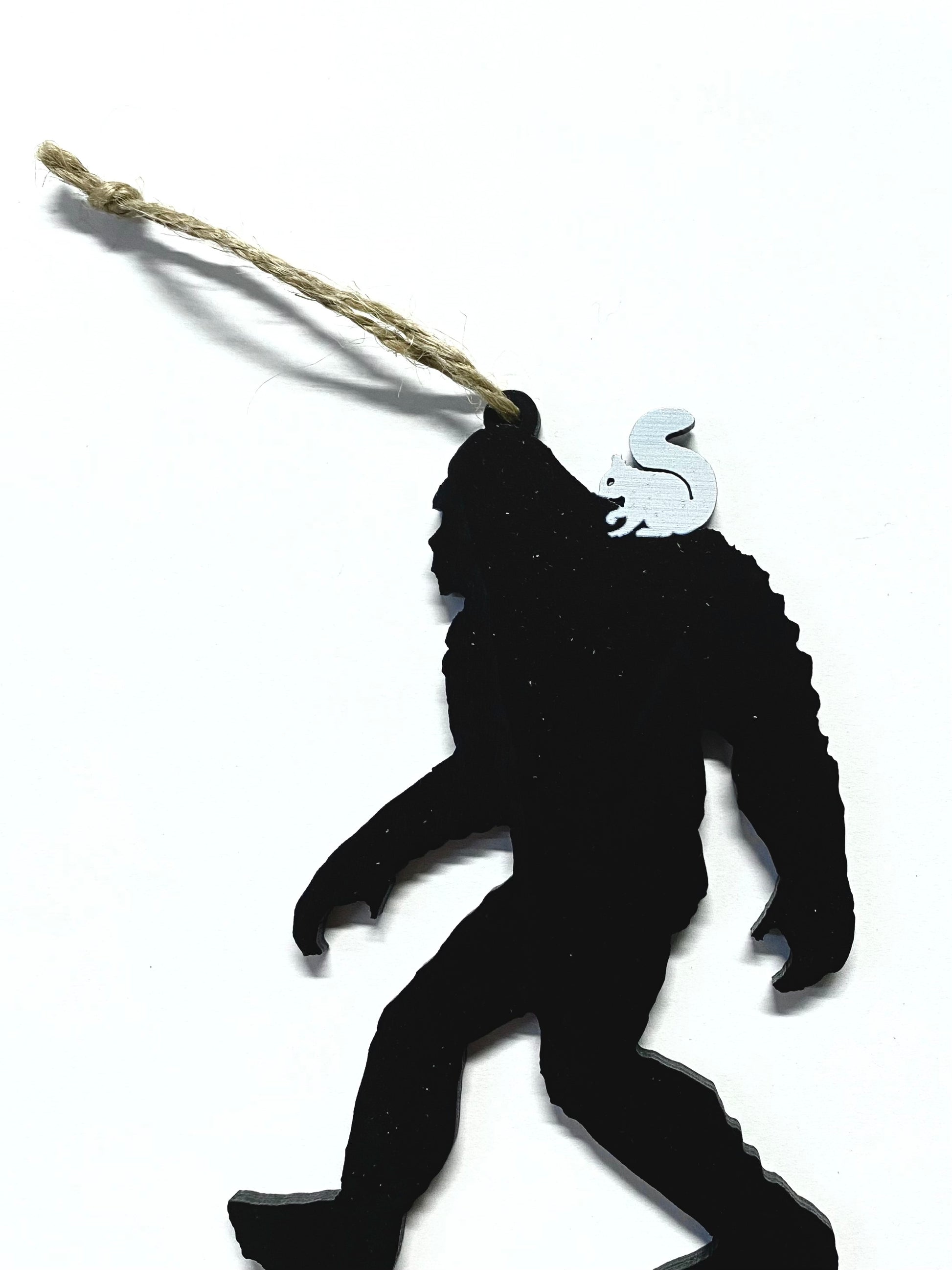 A laser cut wood ornament in the shape of a Sasquatch with a white squirrel on his shoulder. Includes a string attached for hanging.