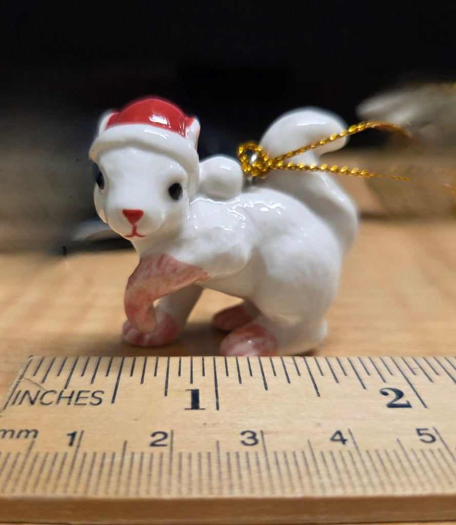 White ceramic squirrel figurine with a red hat shown with ruler for size.