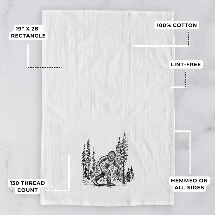 Tea towel with a Sasquatch design on a white background, featuring text about dimensions and material.