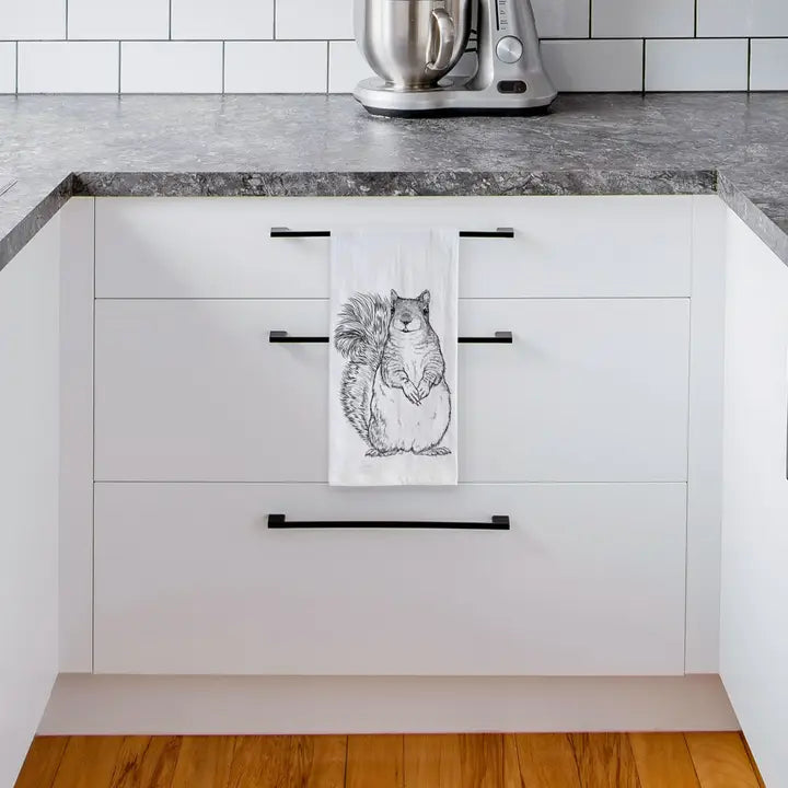 Kitchen with white cabinets, black handles, and a towel with a squirrel design hanging on one of the doors.