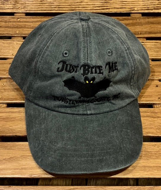 A dark grey baseball cap with 'Just Bite Me' embroidered on the front and a bat silhouette and Transylvania County, NC.