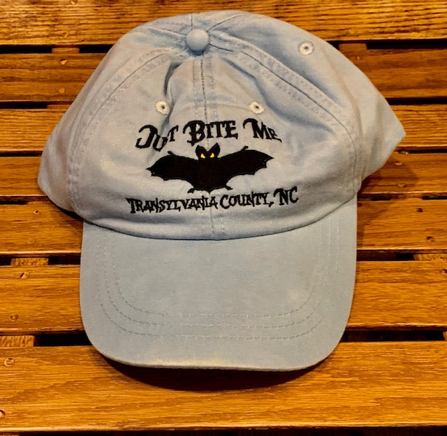 A stone color baseball cap with 'Just Bite Me' embroidered on the front and a bat silhouette and Transylvania County, NC.