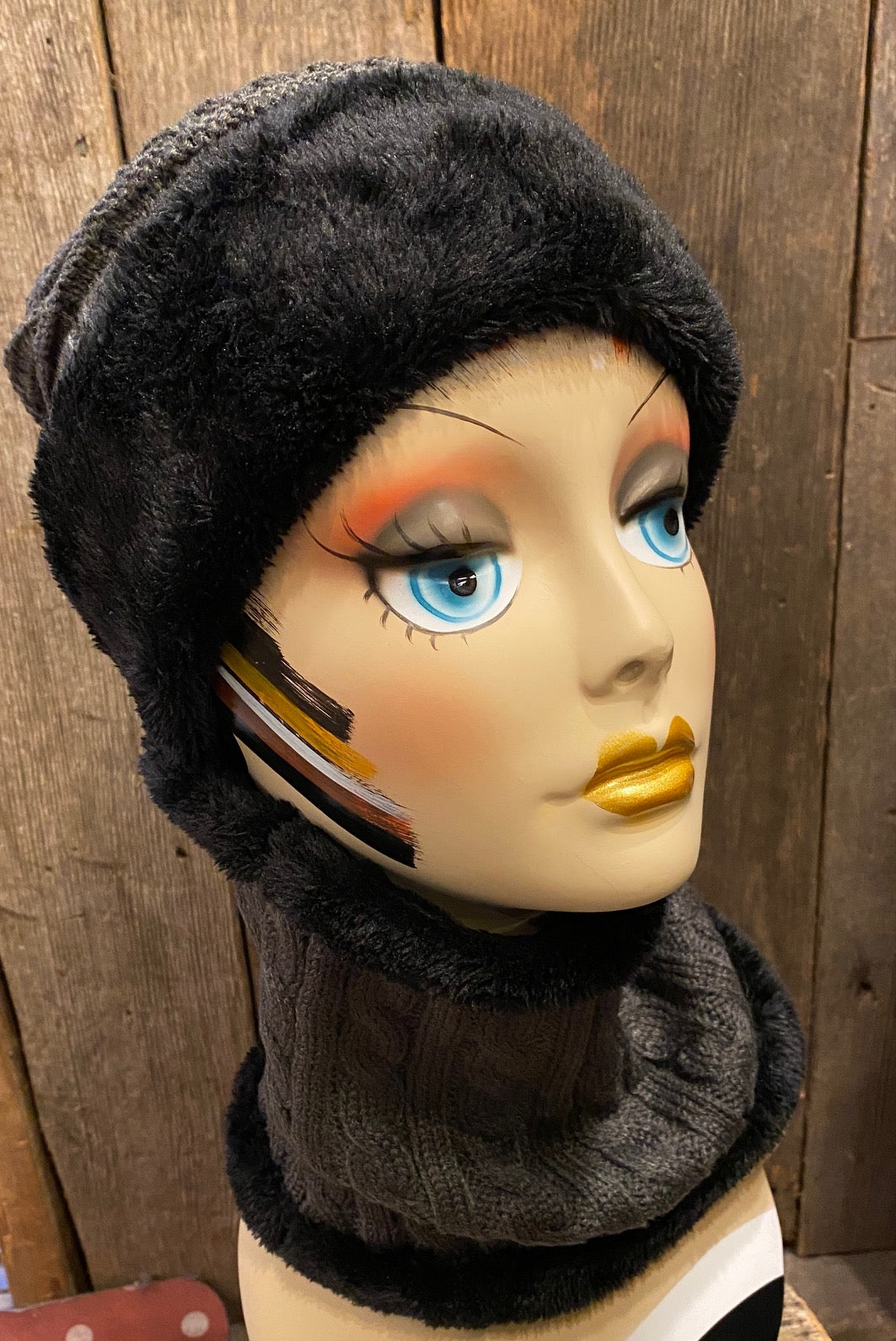 A mannequin head wearing a black cable knit beanie and a matching neck warmer with faux-fur lining.