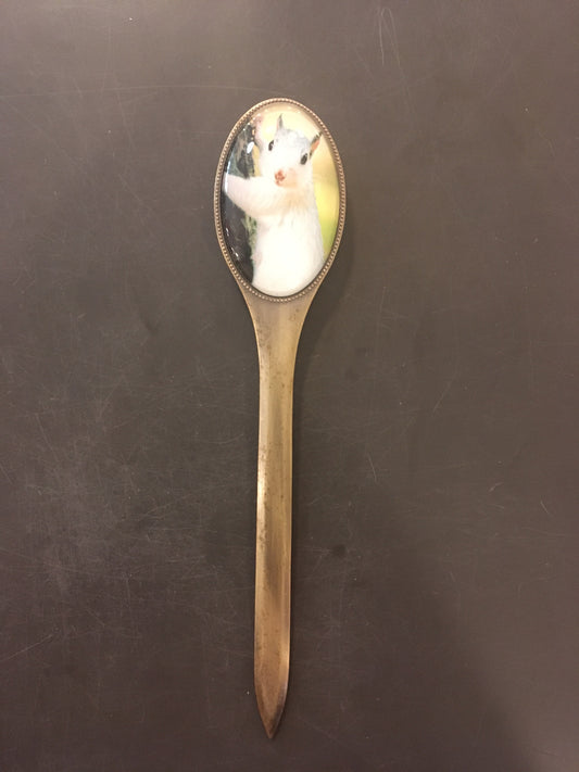A brass letter opener with a glass handle and a two-sided oval picture of a white squirrel on the back side.