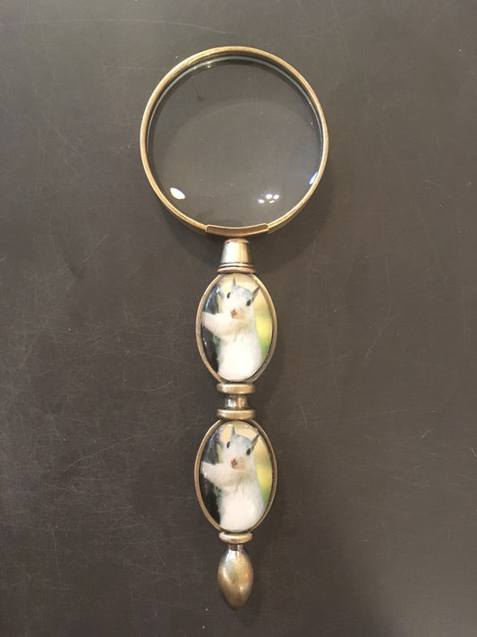 A brass magnifying glass with two white squirrel designs on the handle.