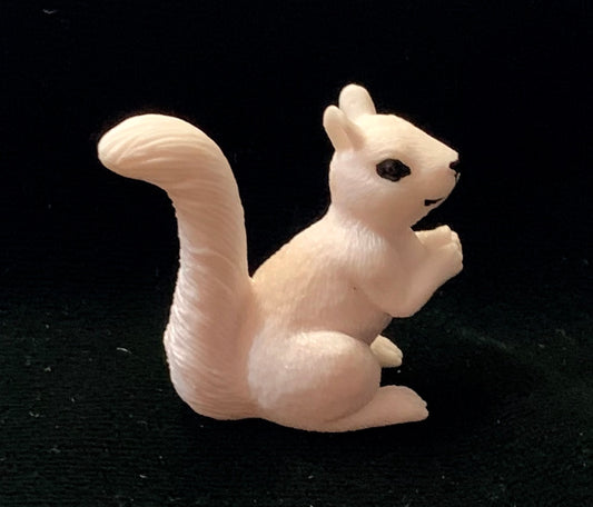 A tiny resin figurine of a white squirrel with a black eye, standing upright.