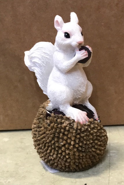A white squirrel resin figurine perched on a half-eaten black walnut.