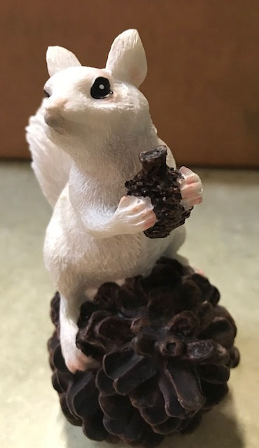 Resin white squirrel perched atop a pine cone