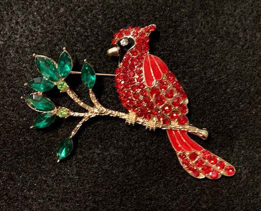 A brooch depicting a red crystal cardinal perched on a branch with green crystals.