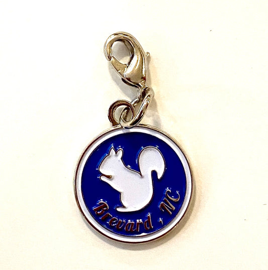 A round metal charm featuring a white squirrel on a blue background with the text 'Brevard, NC'.