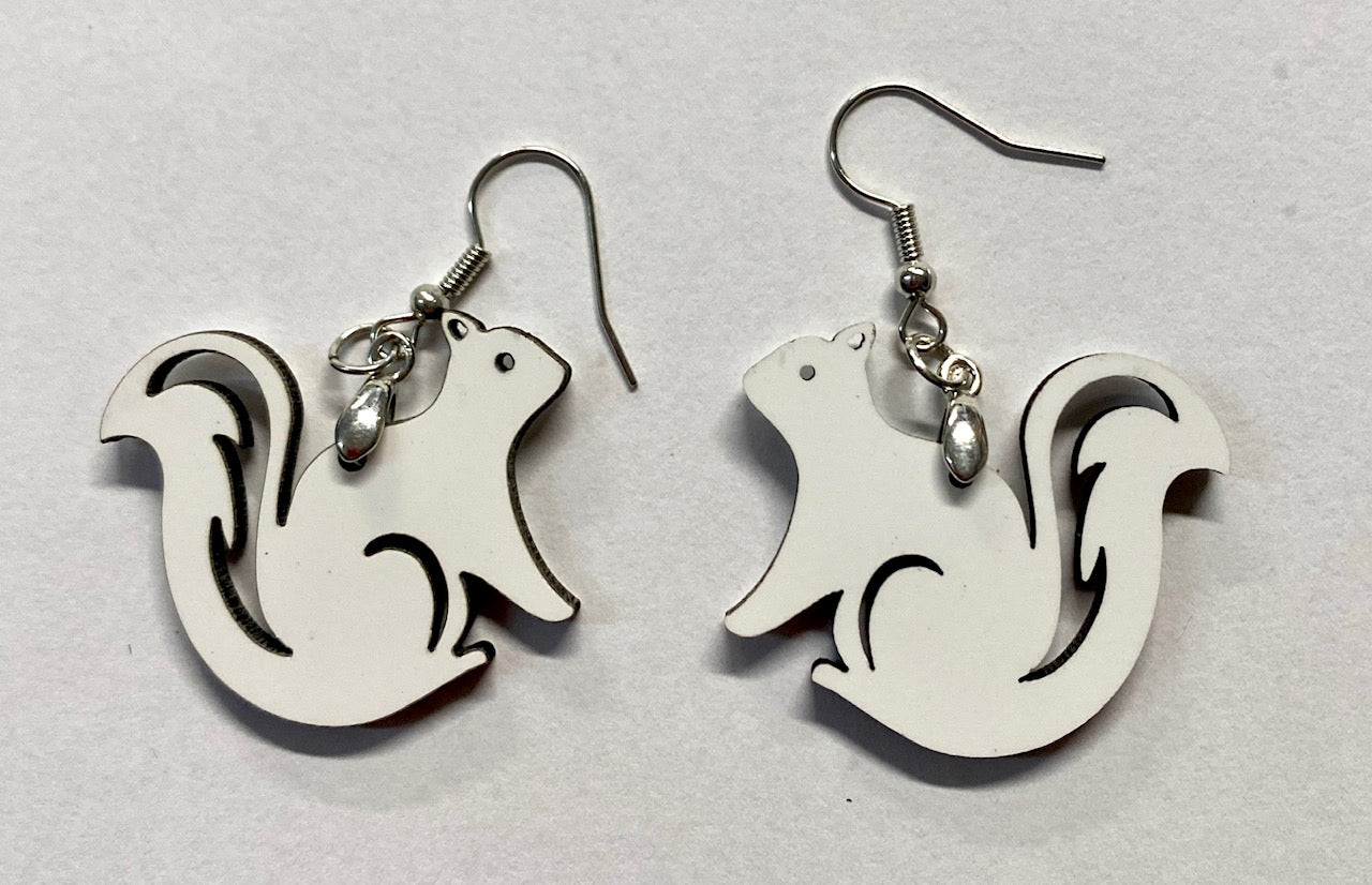 A pair of laser cut wooden earrings in the shape of white squirrels with hollow tail designs.