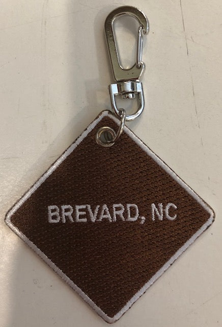 Embroidered key clip with a brown background and 'Brevard, NC' embroidered in white. Square.