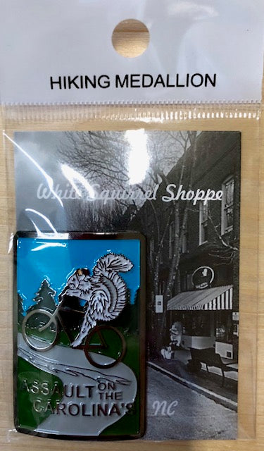 A metal hiking stick medallion with a white squirrel riding a bike, and the text 'Assault on the Carolina's'. 