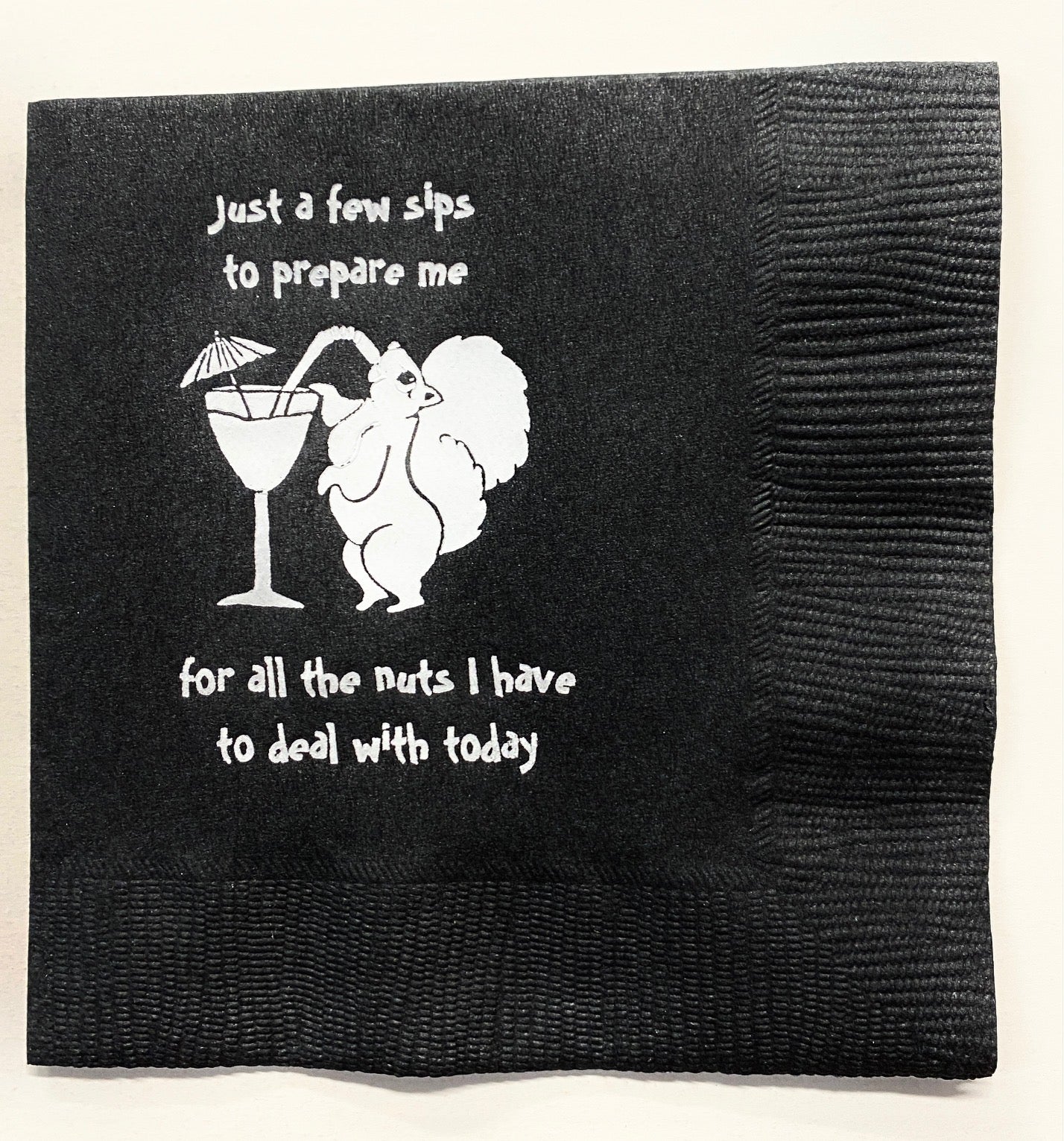 Black cocktail napkin with a white squirrel sipping a martini and saying, "Just a few sips to prepare me for all the nuts I have to deal with today.