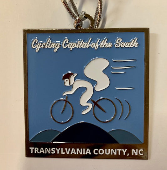 A metal ornament featuring a white squirrel on a bicycle with the text 'Cycling Capital of the South' and 'Transylvania County, NC'.