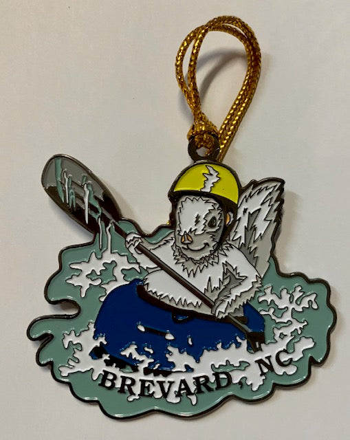 A two-sided metal ornament featuring a white squirrel wearing a yellow helmet, kayaking with the text 'BREVARD, NC'.