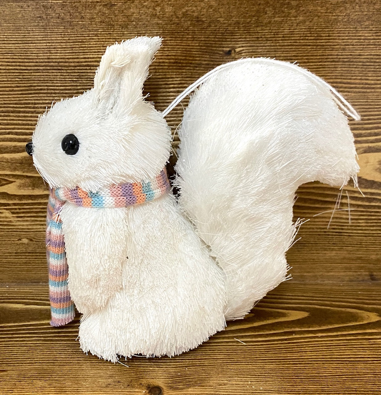 A white sisal squirrel ornament with a pastel striped scarf, profile view.