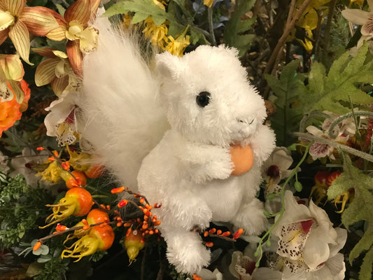 A plush white squirrel with a furry tail holding a small plush acorn.