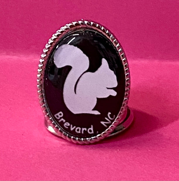 A metal thimble with a white squirrel and the text 'Brevard NC' on a black background.