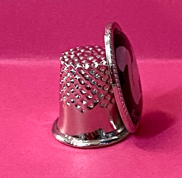 Side view of a collectible metal thimble with a white squirrel emblem on front.