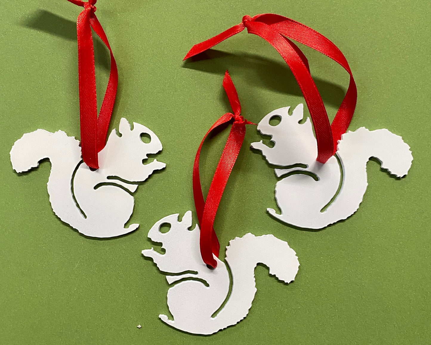 Three white metal die-cut ornaments shaped like squirrels with red satin ribbons for hanging.